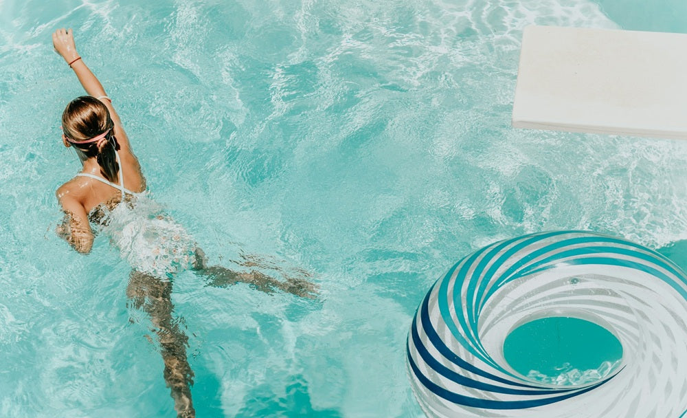 Young girl swimming in a clear pool with a floaty