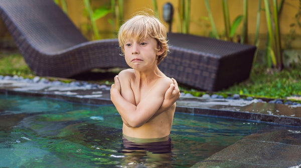 Little boy standing in a cold swimming pool